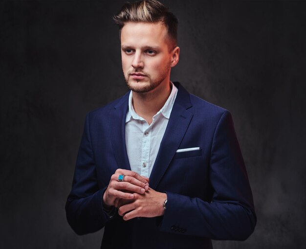 An attractive blond male dressed in a suit over dark grey background.