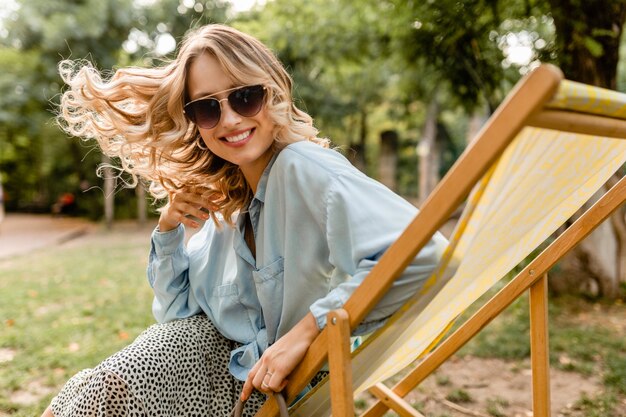 夏の衣装でデッキチェアに座っている魅力的な金髪の笑顔の女性