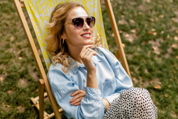 Привлекательная блондинка улыбается женщина сидит расслабленно в шезлонге в стильной одежде