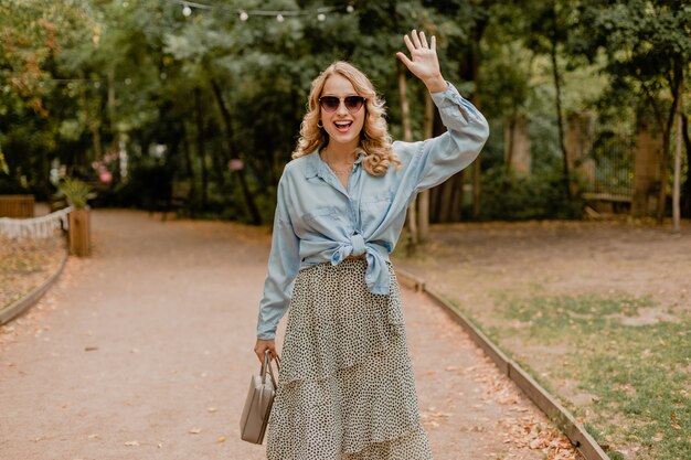 Attractive blond smiling woman walking in park in summer outfit