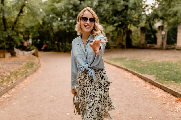 Attractive blond smiling woman walking in park in summer outfit