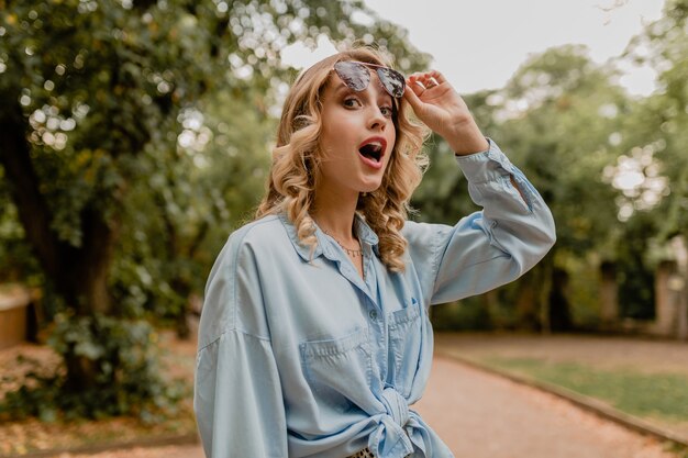 Attractive blond surprised woman walking in park in summer outfit