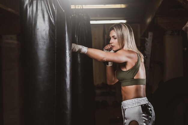 Attractive blond woman has a boxing training with punching bag at kick boxing studio.