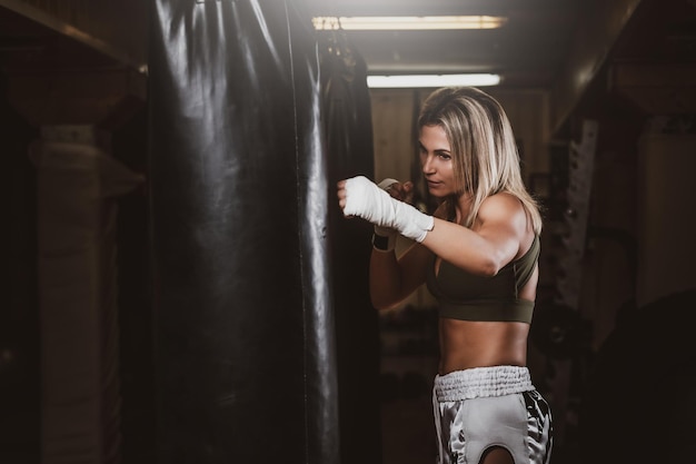 Attractive blond woman has a boxing training with punching bag at kick boxing studio.