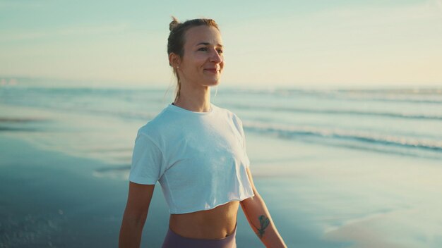 Attractive blond woman looking happy breathing fresh air during walk along the sea after yoga practice Happy girl enjoying morning on beach