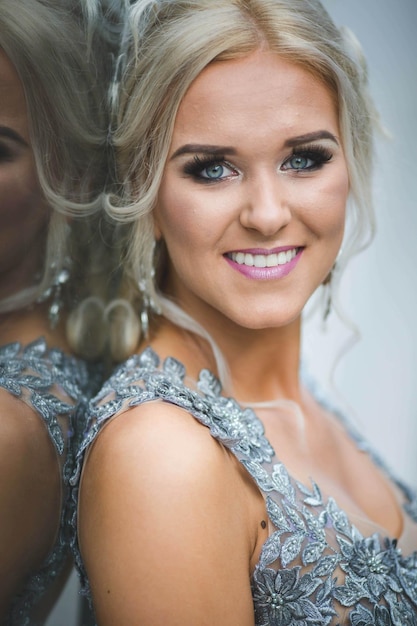 Attractive blonde Caucasian female wearing an elegant long silver dress leaning on a glass building