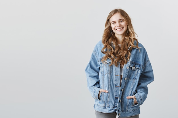Бесплатное фото Привлекательная блондинка колледж девушка в джинсовой куртке улыбается счастливой
