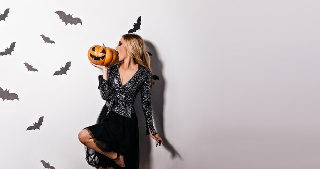 Attractive blonde girl eating halloween pumpkin.  inspired young woman posing in witch attire.