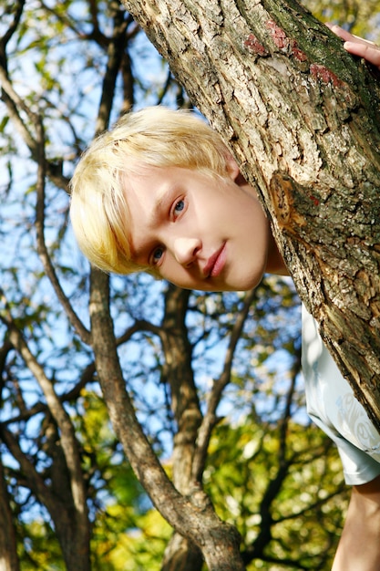 Foto gratuita ragazzo biondo attraente dietro un albero