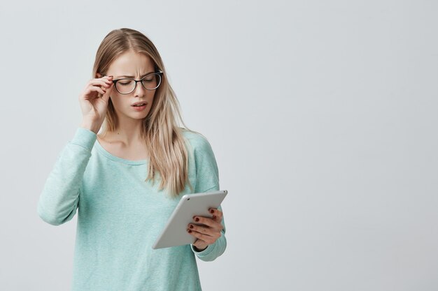 Attractive blonde office worker in eyewear works with digital tablet