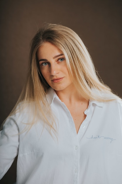 Attractive blonde woman in a white shirt posing on a brown wall