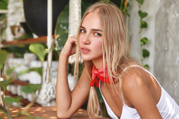 Attractive blonde woman with serious expression, dressed casually, sits in cozy cafe alone