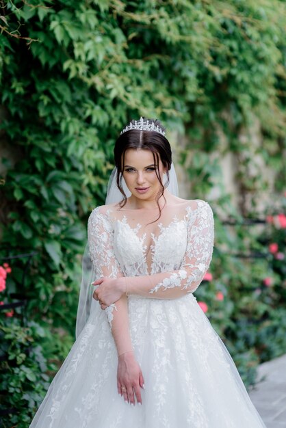 Attractive bride dressed in crown with foxy sight outdoors near green leaves