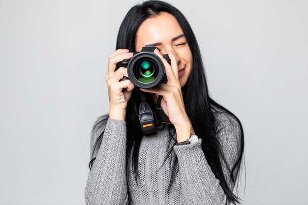 Attractive brunette aims her camera. composing a photograph in studio, isolated on gray wall
