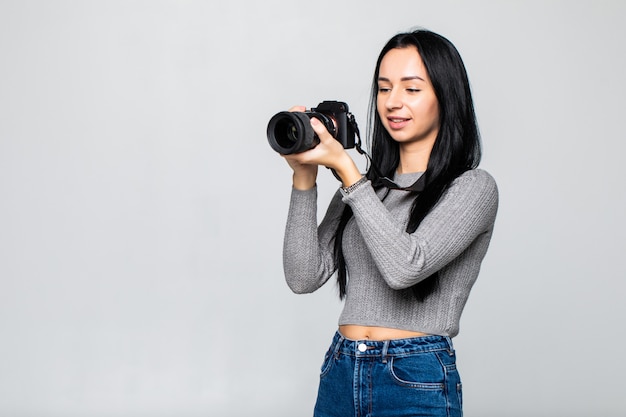 Attractive brunette aims her camera. composing a photograph in studio, isolated on gray wall