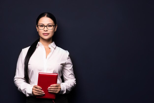 Attractive brunette business woman holding red notebook and posing on camera