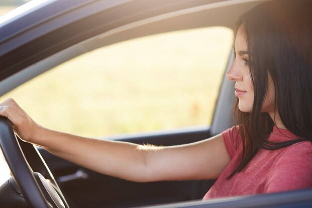 Привлекательная брюнетка-водитель с уверенным выражением лица смотрит на лобовое стекло, наслаждается высокой скоростью и хорошими дорогами