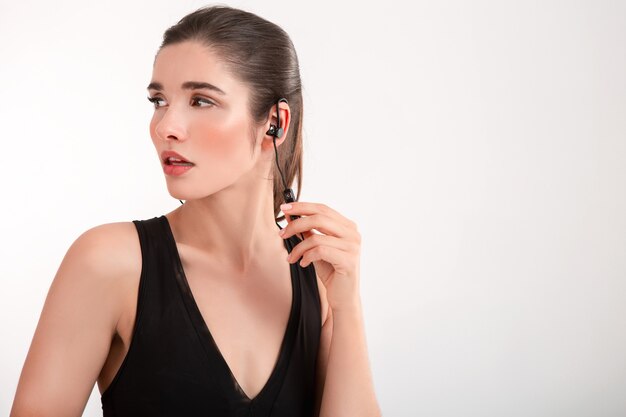 Attractive brunette woman in jogging black top listening to music on earphones posing isolated on white background ponytail hairstyle