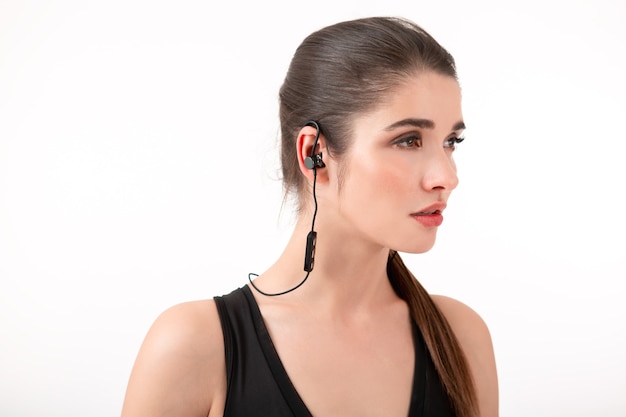 Free photo attractive brunette woman in jogging black top listening to music on earphones posing