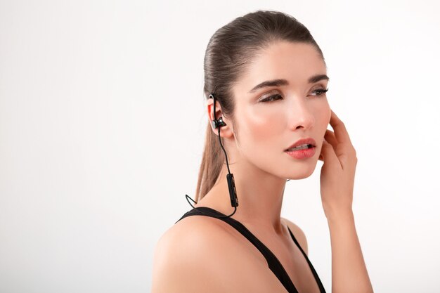 Attractive brunette woman in jogging black top listening to music on earphones posing 