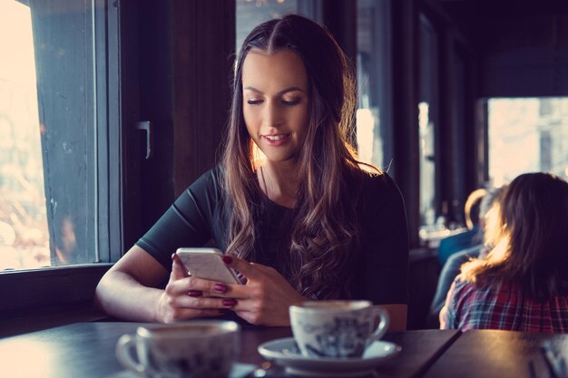 魅力的なブルネットの女性がカフェでSMSにテキストメッセージを送信します。