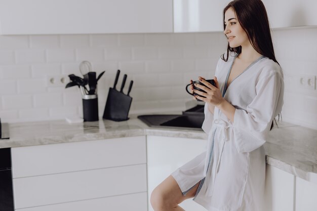 Attractive brunette woman wear in robe making fresh cup of tea or coffee for breakfast. Housewife concept