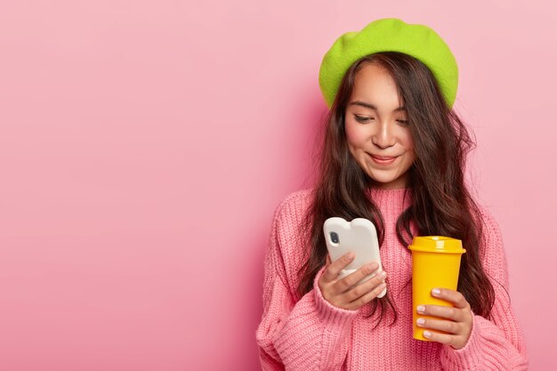 Attractive brunette young Japanese woman holds modern mobile phone, sends text messages in online chat