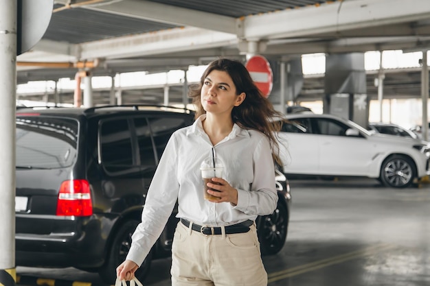 一杯のコーヒーと駐車場で魅力的なビジネスの若い女性