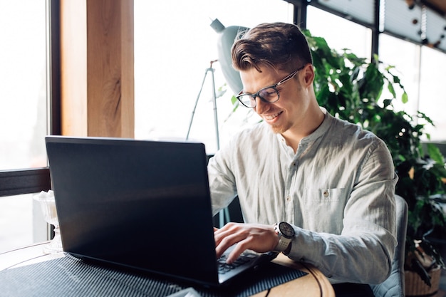 Attractive businessman in eyeglasses working on laptop, typing, spending time at cafe.