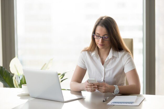 Attractive businesswoman holding smartphone, texting message