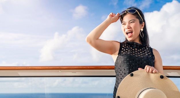 魅力的なのんきなアジアの女性の女性のカジュアルな服の笑顔は、青い空の雲の背景を持つクルーズ船のバルコニーで喜びの休暇の時間をリラックスします