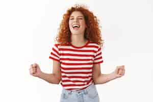 Free photo attractive carefree lively redhead curly woman enjoy having fun release emotions dancing close eyes scream yes thrilled clench fists triumphing winning lottery