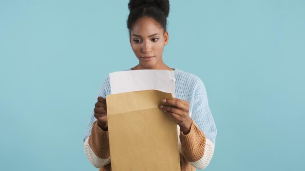 Attractive casual african american girl intently opening envelope with exams results over colorful background