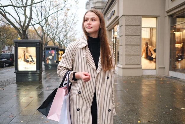 Привлекательная случайная девушка уверенно ходит по дождливой городской улице с сумками для покупок