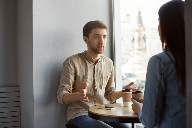 검은 머리와 다름 그의 작품에 대 한 그의 여자 친구와 얘기 하 고 손으로 한순간 하 고 커피를 마시는 날짜에 카페에 앉아 매력적인 백인 남자.