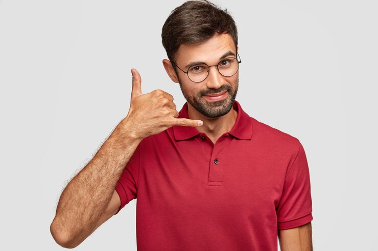 Free Photo attractive caucasian young male in casual clothes imitates telephone conversation, keeps hand near ear as if holding mobile phone, has confident facial expression, isolated over white wall.