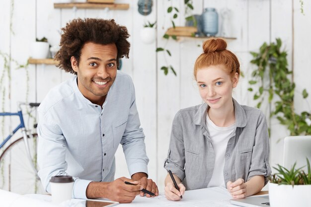 Attractive cheerful dark-skinned engineer with Afro hairstyle and his cute redhead female colleague