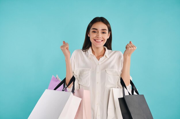 Attractive cheerful girl with shopping bags rejoicing on camera over colorful background isolated