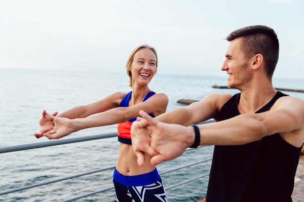 Attractive cheerful young couple doing stretching exercises for arms while working out