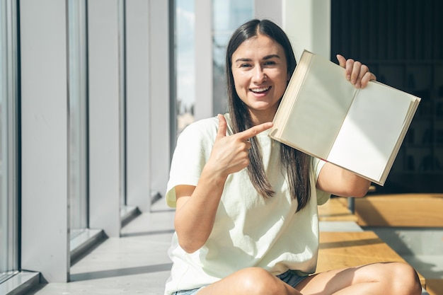 Free photo attractive cheerful young woman at the window with an open book