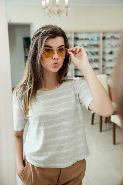 Attractive confident girl trying on stylish eyewear while on shopping in optician store