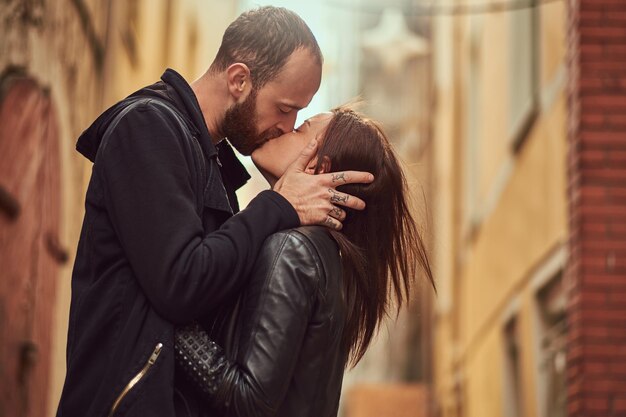 Attractive couple, bearded man and brunette girl kissing outside old European street on a background.
