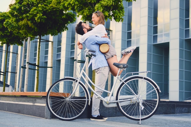 Attractive couple on a date after bicycle ride in a city. A man hugs a woman over modern building background.