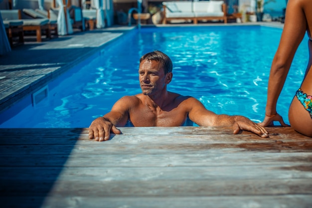 An attractive couple, handsome muscular male and sexy woman sitting near the pool and enjoying a vacation.