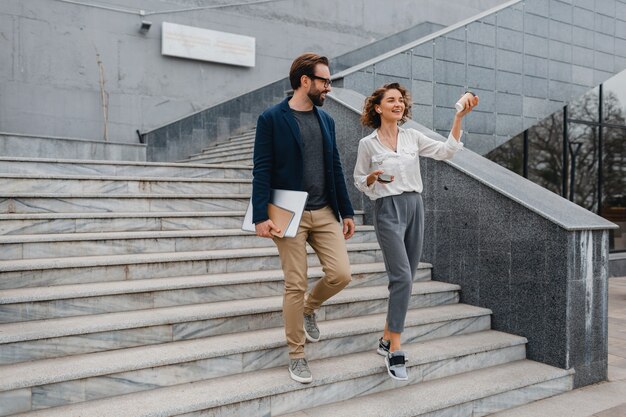 Attractive couple of man and woman going on stairs in urban city center, holding laptop, discussing