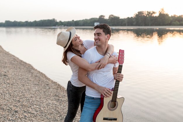 Привлекательная пара гуляет у озера с гитарой