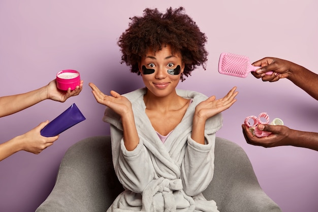 Attractive curly haired woman in bathrobe, spreads palms sideways