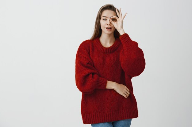 Attractive dreamy girl has everything under control. Portrait of sexy charming caucasian female model in stylish loose sweater, showing ok or great gesture over eye and gazing sensually 