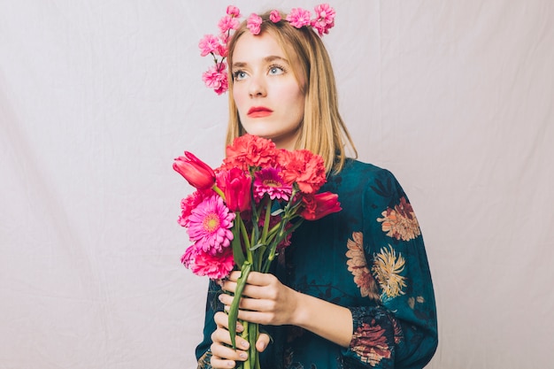 Attractive dreamy sensual woman with wreath on head and bouquet of flowers