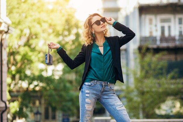 Attractive elegant woman walking in city street with purse, wearing black jacket, confident and sexy,